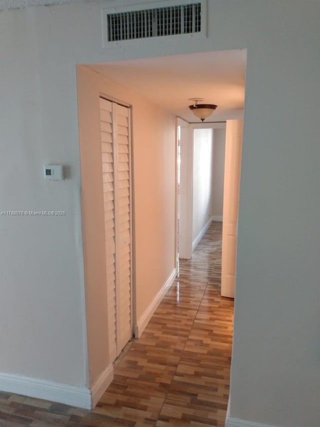 corridor with baseboards, wood finished floors, and visible vents
