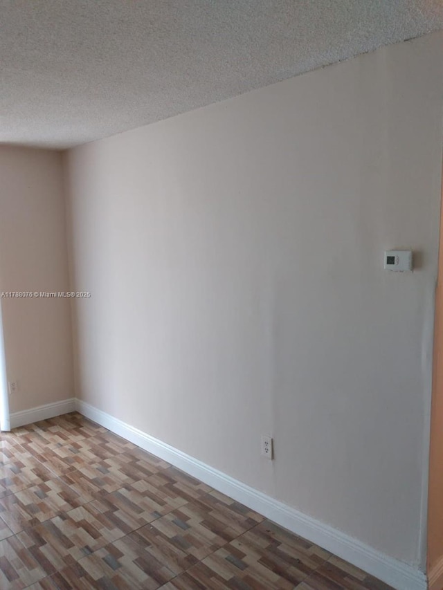 spare room featuring baseboards, wood finished floors, and a textured ceiling