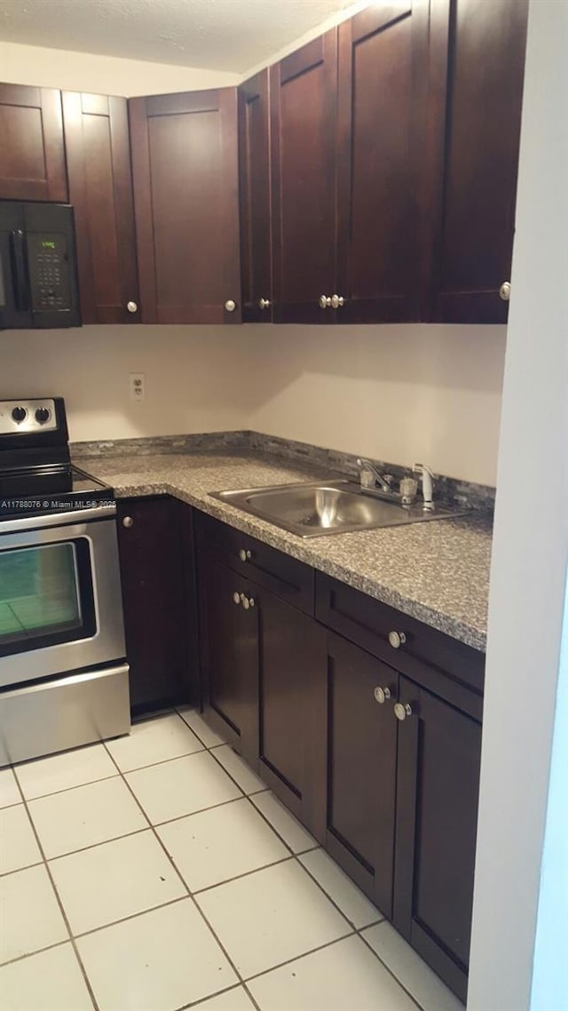 kitchen with dark countertops, a sink, black microwave, light tile patterned floors, and electric range