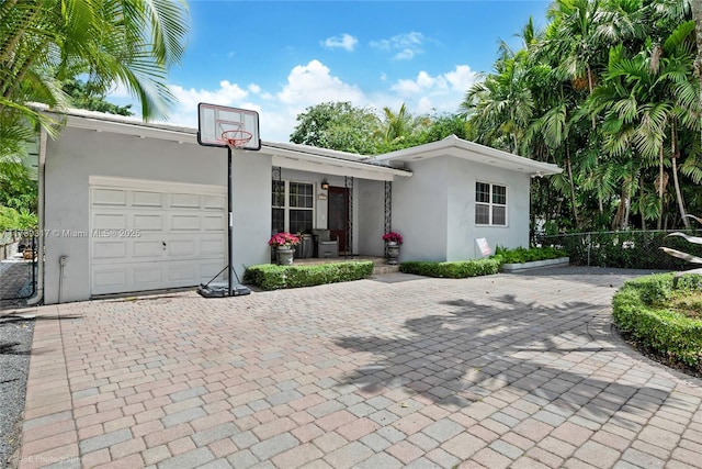 ranch-style house featuring decorative driveway, a garage, stucco siding, and fence