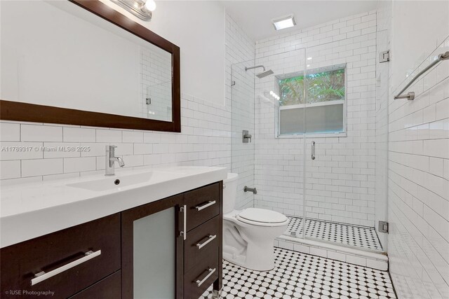 bathroom with tile walls, vanity, toilet, a stall shower, and tile patterned flooring