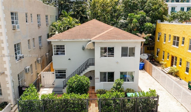 view of front of home featuring stairway, a fenced backyard, roof with shingles, an AC wall unit, and stucco siding