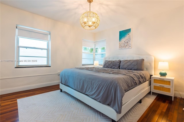 bedroom with an inviting chandelier, dark wood-style flooring, and baseboards