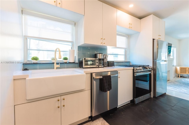 kitchen featuring a sink, decorative backsplash, stainless steel appliances, light countertops, and white cabinets