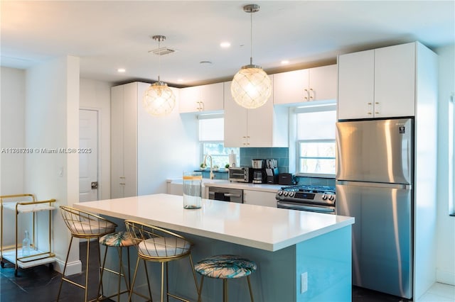 kitchen featuring appliances with stainless steel finishes, light countertops, white cabinetry, a center island, and a kitchen breakfast bar