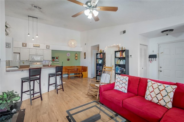 living room with a textured ceiling, visible vents, a ceiling fan, and light wood-style flooring