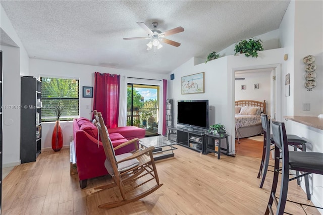 living area featuring lofted ceiling, a textured ceiling, ceiling fan, and light wood-style flooring