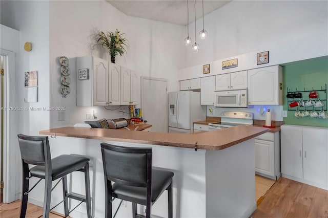 kitchen with a breakfast bar area, white cabinetry, a towering ceiling, white appliances, and a peninsula