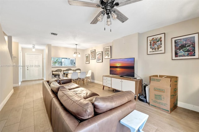 living room with light wood-style flooring, visible vents, a ceiling fan, and baseboards
