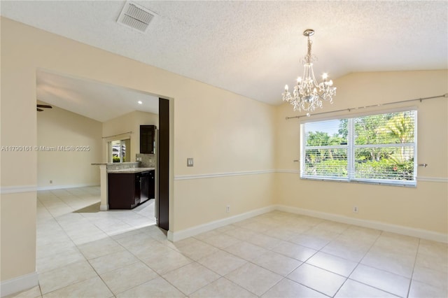 spare room featuring a notable chandelier, lofted ceiling, light tile patterned flooring, and visible vents