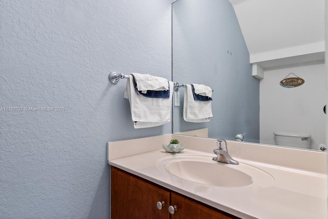 bathroom with a textured wall, toilet, and vanity