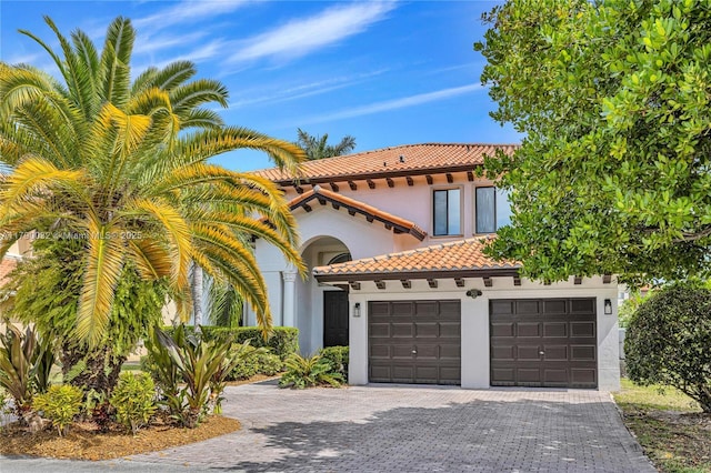 mediterranean / spanish-style house with a tile roof, decorative driveway, stucco siding, and a garage