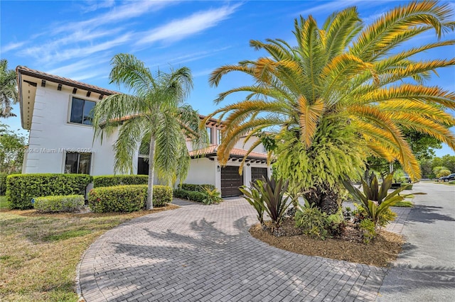 view of front of property featuring stucco siding, decorative driveway, a tiled roof, and a garage