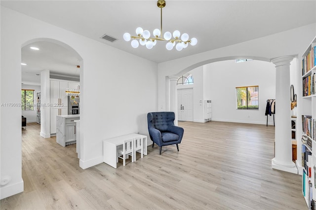 sitting room with arched walkways, decorative columns, light wood-type flooring, baseboards, and visible vents