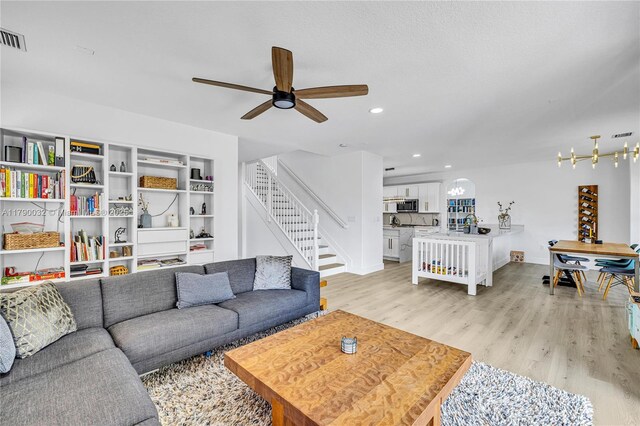 living room with baseboards, light wood-type flooring, ceiling fan with notable chandelier, and stairs