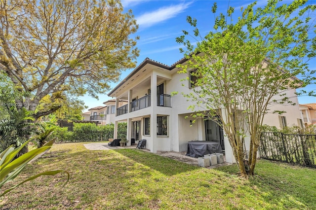 rear view of property with fence, a yard, stucco siding, and a balcony