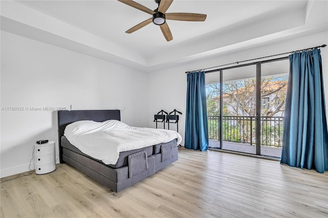 bedroom with wood finished floors, access to outside, baseboards, a ceiling fan, and a tray ceiling