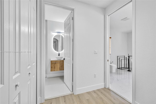 hallway featuring baseboards, light wood-type flooring, visible vents, and a sink