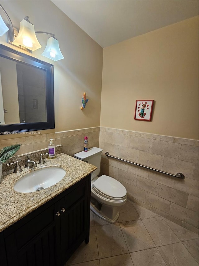 half bathroom with tile patterned floors, toilet, tile walls, wainscoting, and vanity