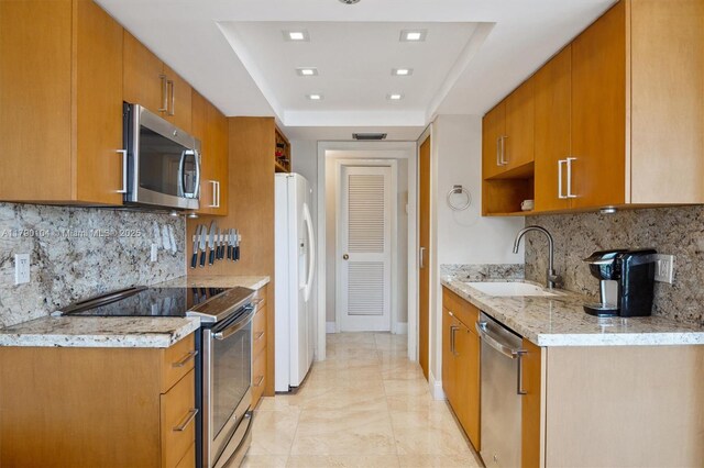 kitchen with a sink, brown cabinets, a tray ceiling, stainless steel appliances, and backsplash