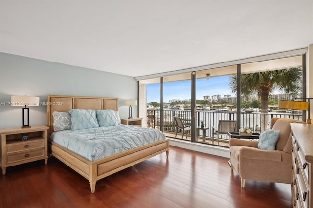 bedroom with expansive windows, wood finished floors, a water view, and access to outside