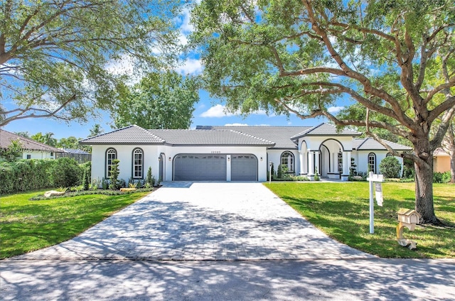 view of front of home featuring a tile roof, decorative driveway, a garage, a front yard, and stucco siding