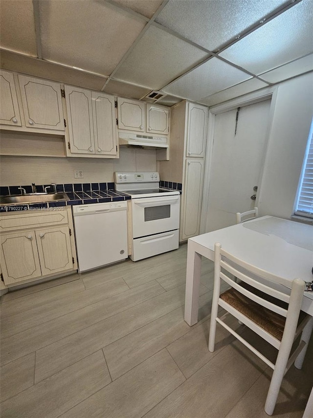 kitchen with a sink, tile counters, under cabinet range hood, light wood-type flooring, and white appliances
