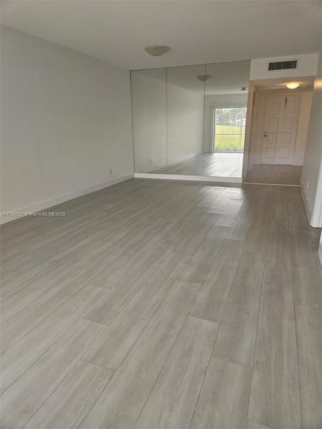 spare room with wood finished floors, visible vents, and baseboards
