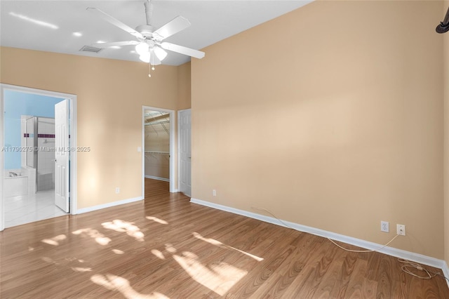 unfurnished bedroom featuring a spacious closet, wood finished floors, a closet, baseboards, and visible vents