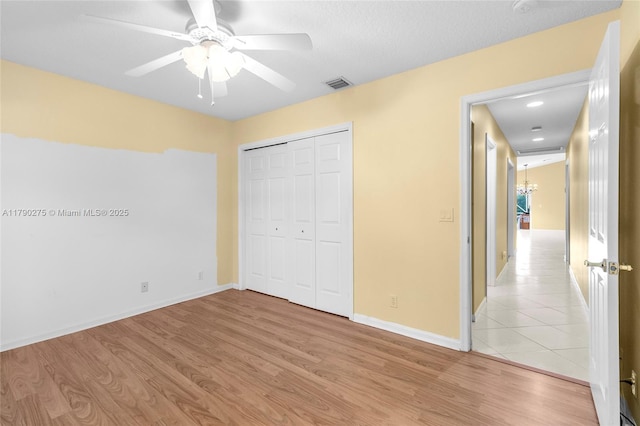 unfurnished bedroom with visible vents, light wood-type flooring, baseboards, and a closet
