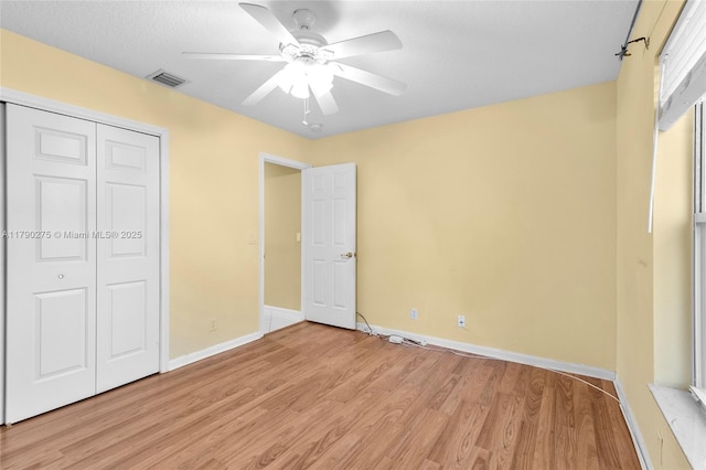 unfurnished bedroom featuring a closet, light wood-type flooring, a ceiling fan, visible vents, and baseboards