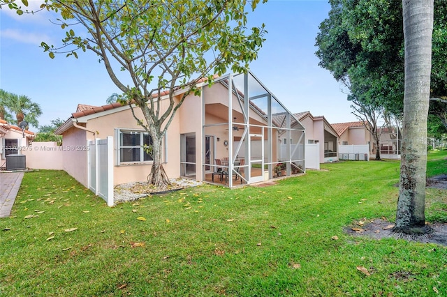 rear view of house with stucco siding, fence, cooling unit, and a yard