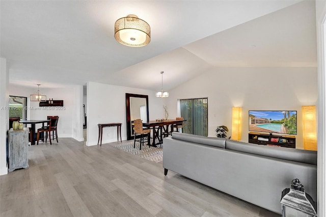 living room featuring light wood finished floors, vaulted ceiling, a chandelier, and baseboards