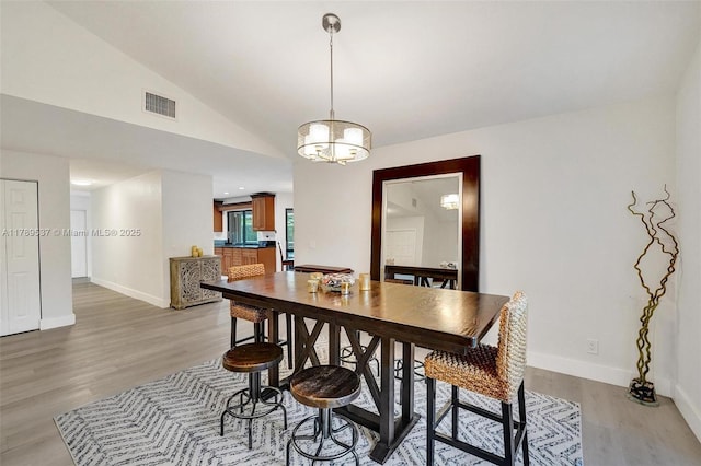 dining space featuring light wood-style flooring, baseboards, lofted ceiling, and a chandelier