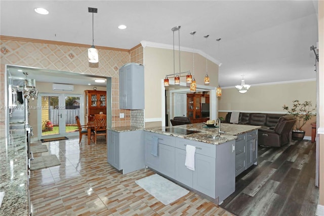kitchen featuring light stone counters, gray cabinets, open floor plan, a wall mounted AC, and ornamental molding