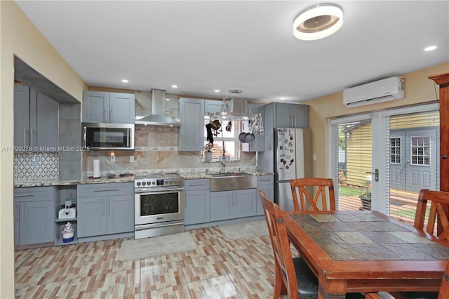 kitchen with wall chimney range hood, appliances with stainless steel finishes, a sink, a wall mounted air conditioner, and tasteful backsplash