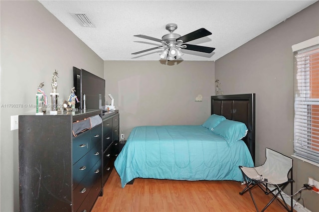 bedroom featuring light wood-style floors, a textured ceiling, ceiling fan, and visible vents