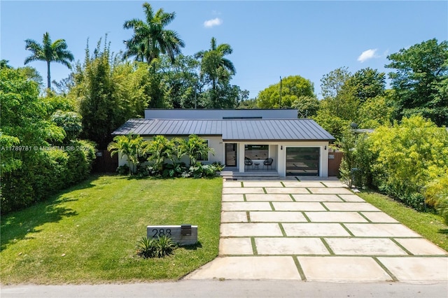 view of front facade featuring driveway, a standing seam roof, a front yard, and metal roof
