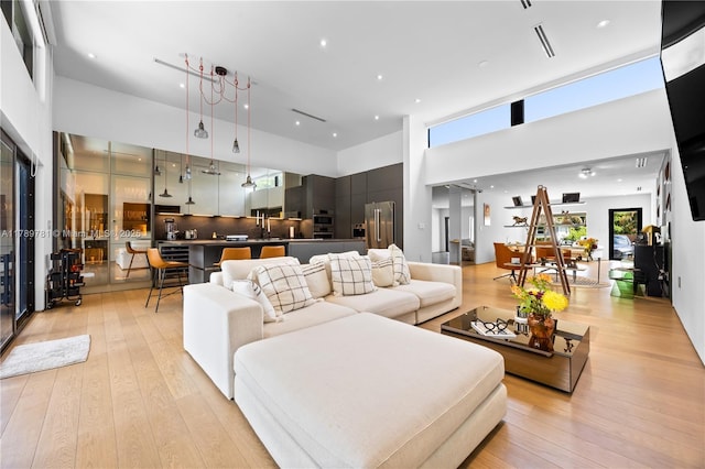 living room featuring a towering ceiling, visible vents, light wood-type flooring, and recessed lighting