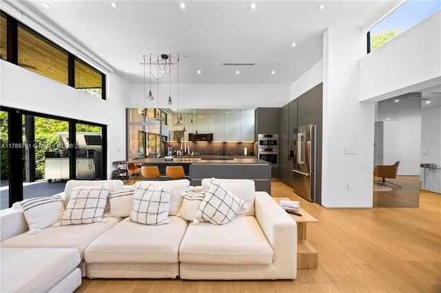 living room featuring recessed lighting, a wealth of natural light, a high ceiling, and light wood finished floors