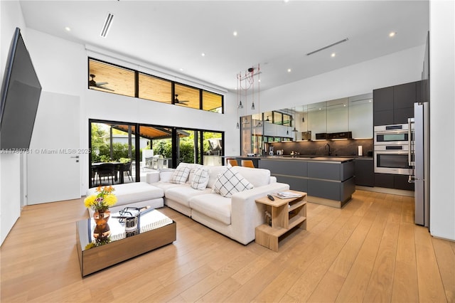 living room featuring a towering ceiling, light wood-style floors, and recessed lighting