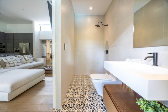bathroom with a sink, a tile shower, toilet, and tile walls