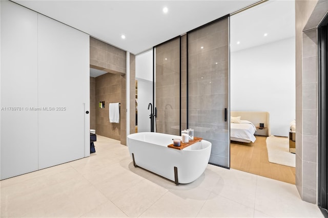 ensuite bathroom with recessed lighting, ensuite bath, tile patterned flooring, a freestanding bath, and tile walls