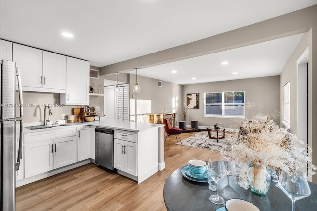 kitchen with a peninsula, appliances with stainless steel finishes, a sink, and white cabinetry