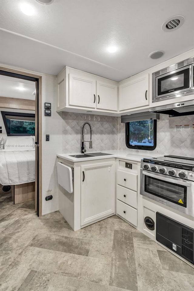kitchen featuring white cabinets, a sink, stainless steel microwave, decorative backsplash, and light countertops