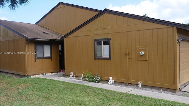 view of side of home featuring a lawn and a shingled roof