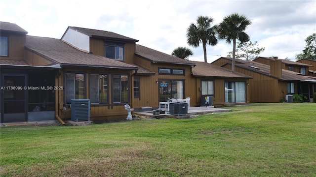 rear view of property featuring a sunroom, a lawn, a shingled roof, and central AC unit