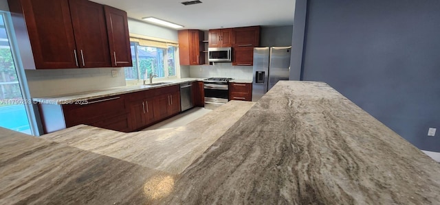 kitchen with a sink, stainless steel appliances, decorative backsplash, visible vents, and reddish brown cabinets
