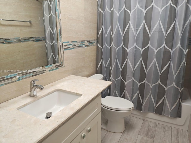 bathroom with shower / bath combo with shower curtain, toilet, tile walls, wood finished floors, and vanity