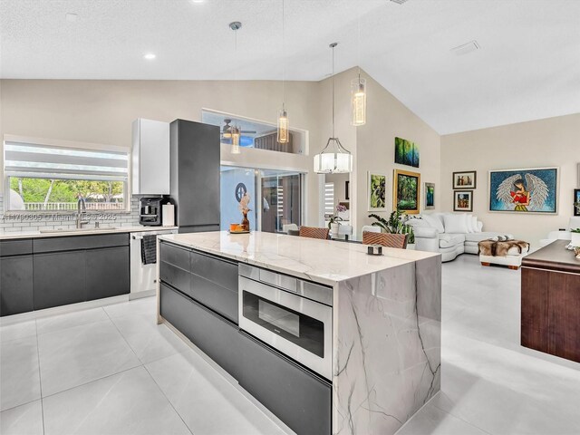 kitchen featuring modern cabinets, a sink, light stone countertops, a center island, and high vaulted ceiling